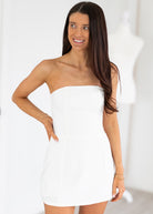 Woman wearing a white strapless dress against a plain background