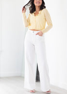Woman wearing a yellow cropped top and white wide-leg pants against a white background