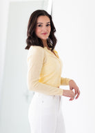 Woman wearing a yellow long-sleeve top and white pants against a white background