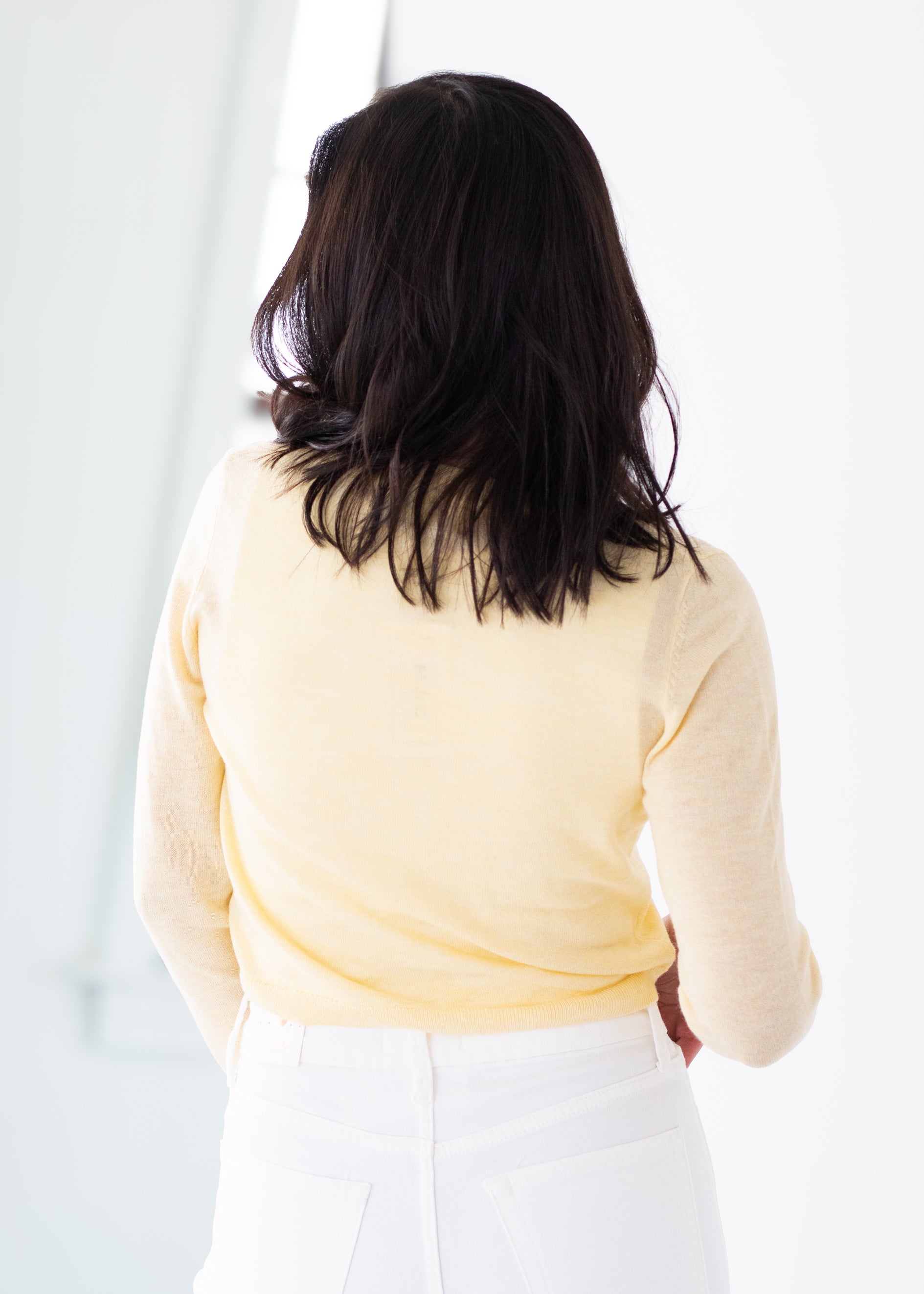 Person wearing a light yellow sweater and white pants against a plain background