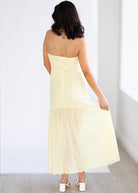 Woman wearing a light yellow strapless dress against a white background