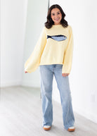 Woman wearing a yellow sweater with a fish design and blue jeans on a white background