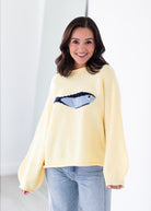Woman wearing a yellow sweater with a blue graphic design on a white background