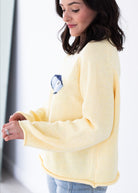 Woman wearing a light yellow sweater with a blue and white pattern on a white background