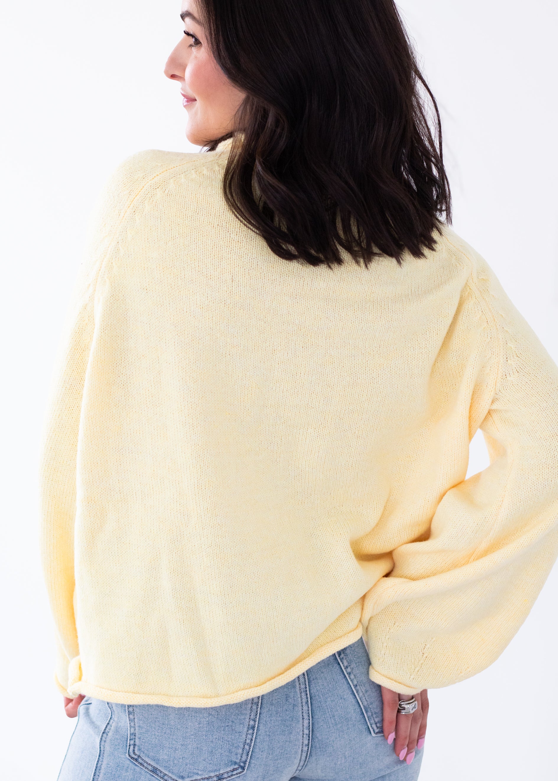 Woman wearing a light yellow sweater and blue jeans on a white background
