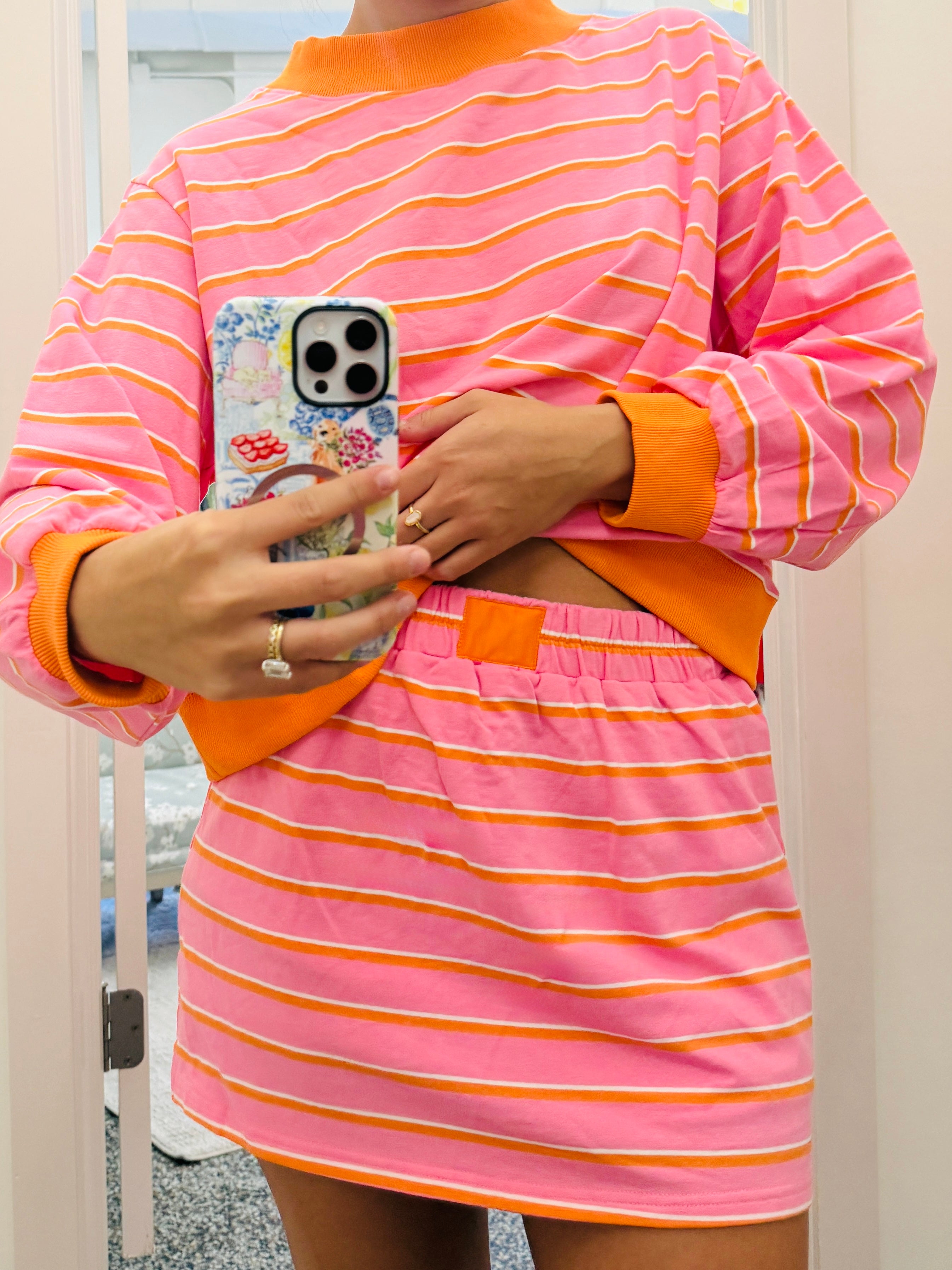 Person wearing a pink and orange striped outfit holding a phone.