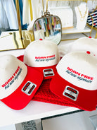 Three red and white caps with 'Born Free but now expensive' text on a table.