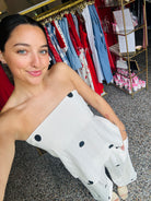 Woman holding a white garment with black dots in a clothing store.