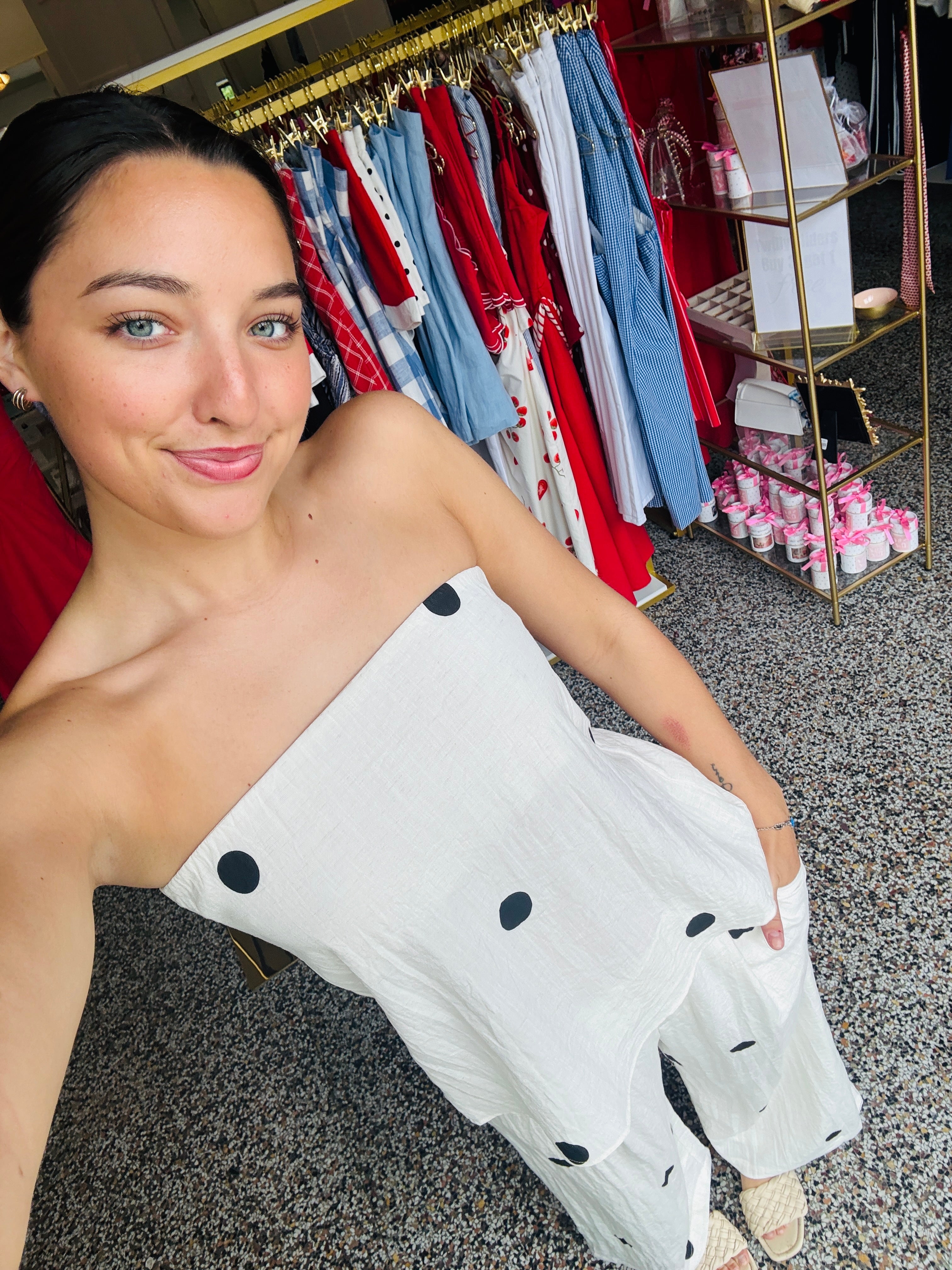 Woman holding a white garment with black dots in a clothing store.
