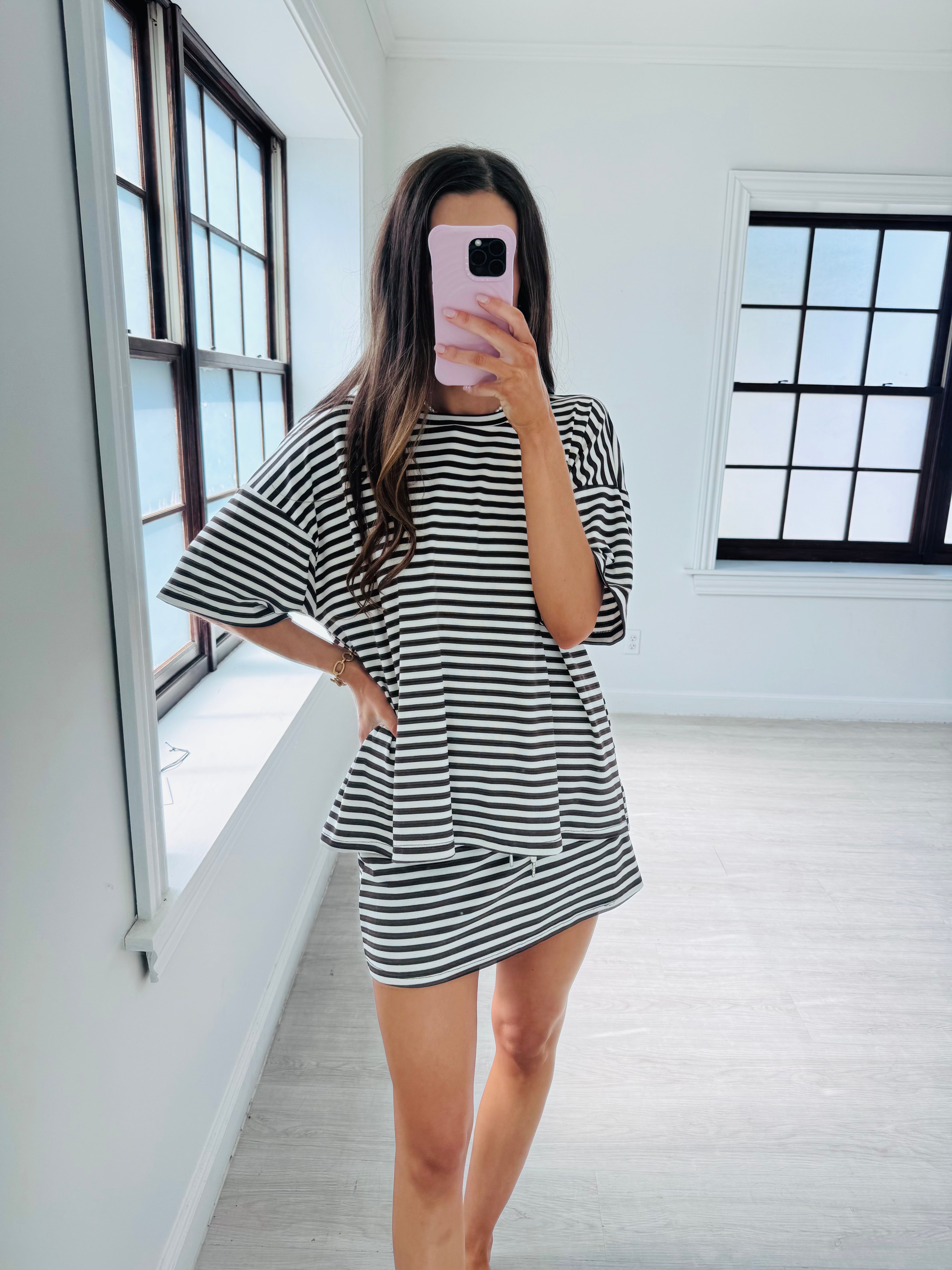 A woman takes a mirror selfie in a bright room wearing a black and white horizontally striped tunic top and matching mini skirt set.
