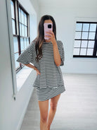 A woman takes a mirror selfie in a bright room wearing a black and white horizontally striped tunic top and matching mini skirt set.
