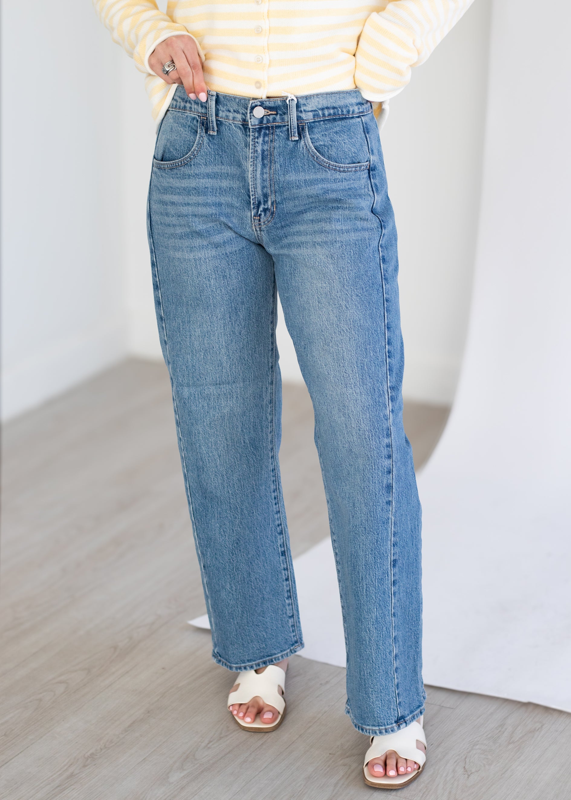 Person wearing blue jeans and a yellow striped shirt on a light wooden floor.