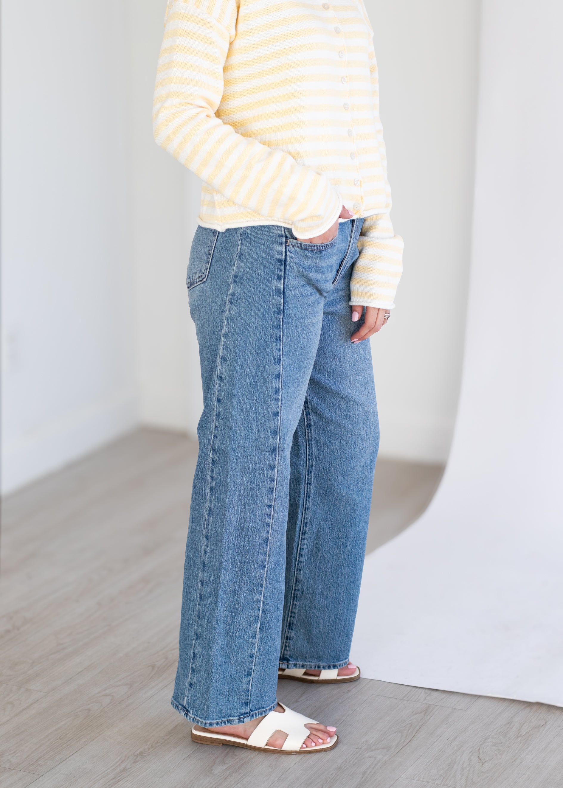 Person wearing a yellow striped shirt and blue jeans standing against a plain white background