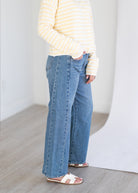 Person wearing a yellow striped shirt and blue jeans standing against a plain white background