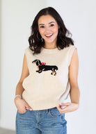 Woman wearing a cream-colored sleeveless sweater with a dachshund design on a plain background