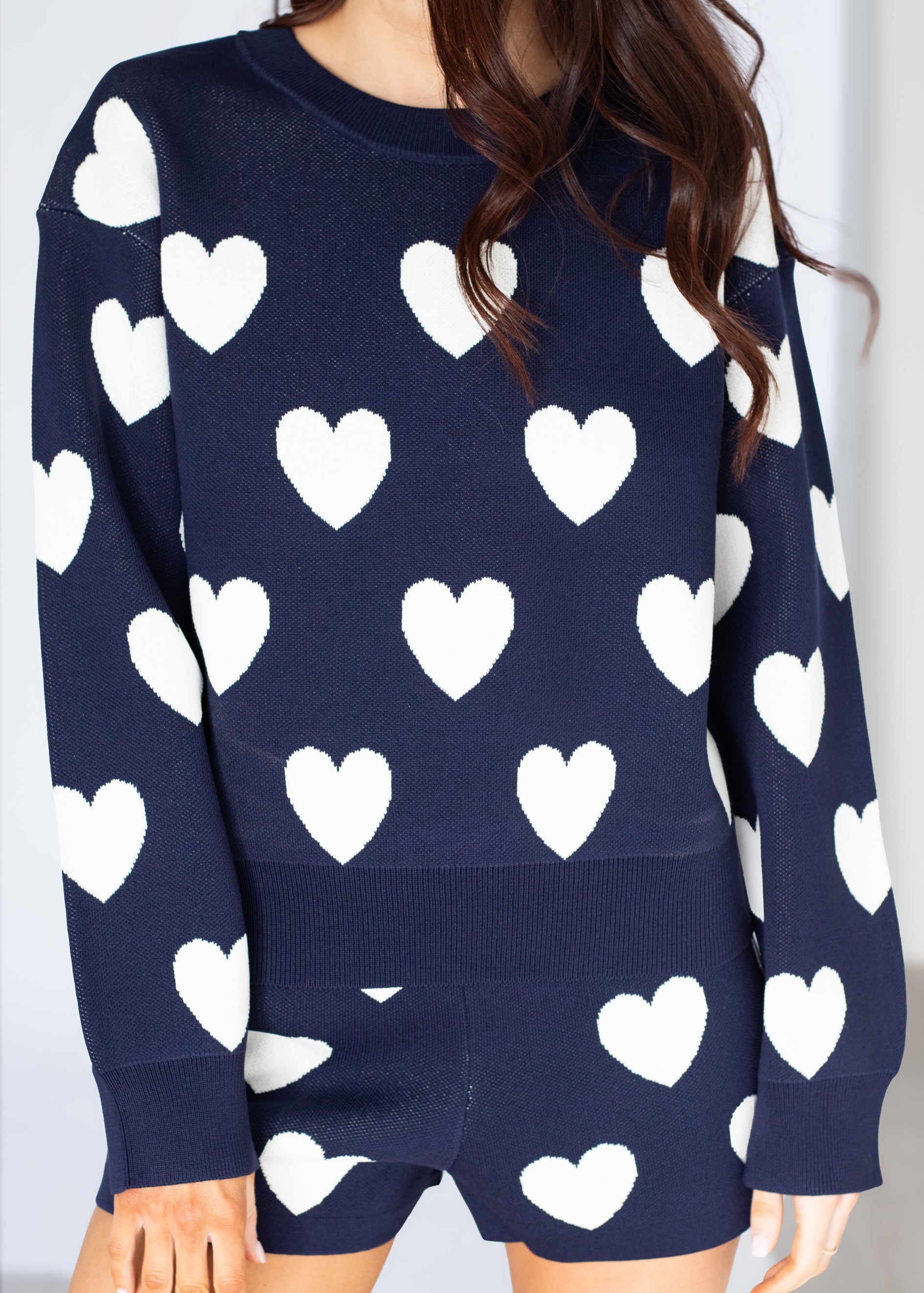 Navy sweater with white heart patterns worn by a person against a plain background