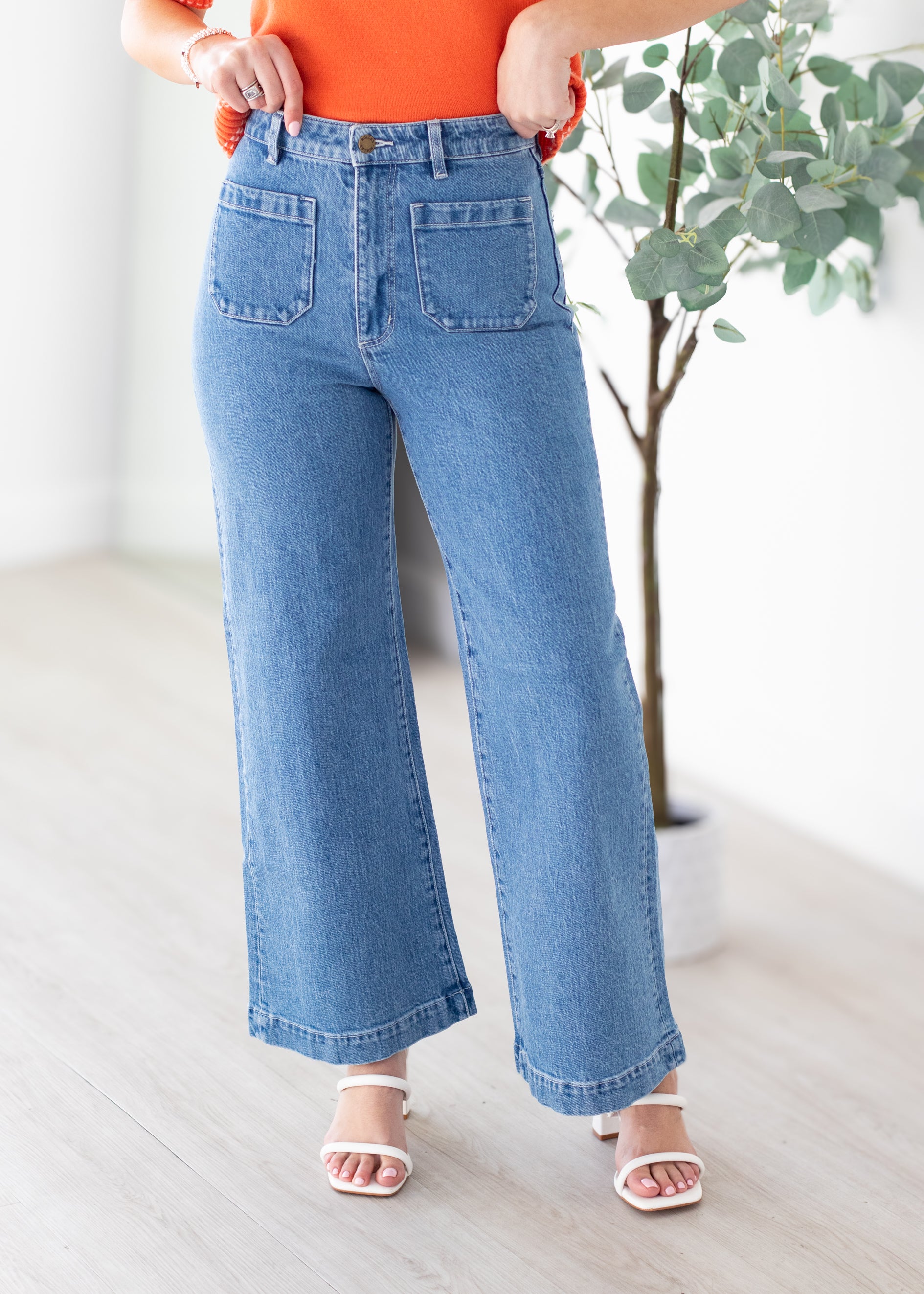 Person wearing blue wide-leg jeans with an orange top in a minimal indoor setting.