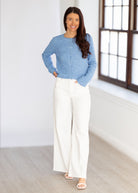 Woman wearing a blue sweater and white pants in a bright room.