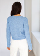 Person wearing a blue sweater and white pants against a white background