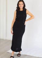 Woman wearing a black sleeveless top and quilted skirt against a white background