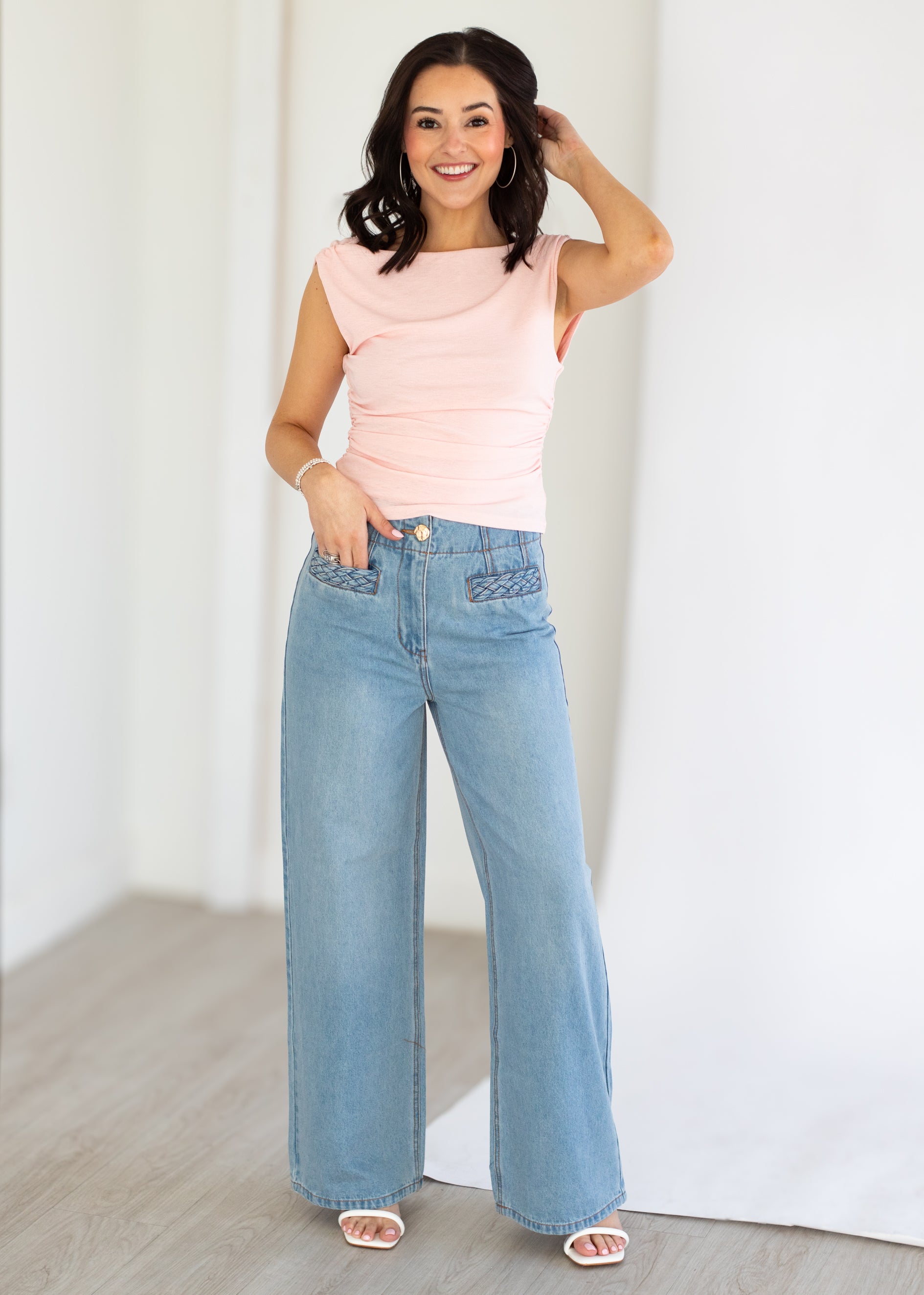 Woman wearing a pink sleeveless top and blue jeans against a white background