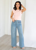Woman wearing a pink sleeveless top and blue jeans against a white background