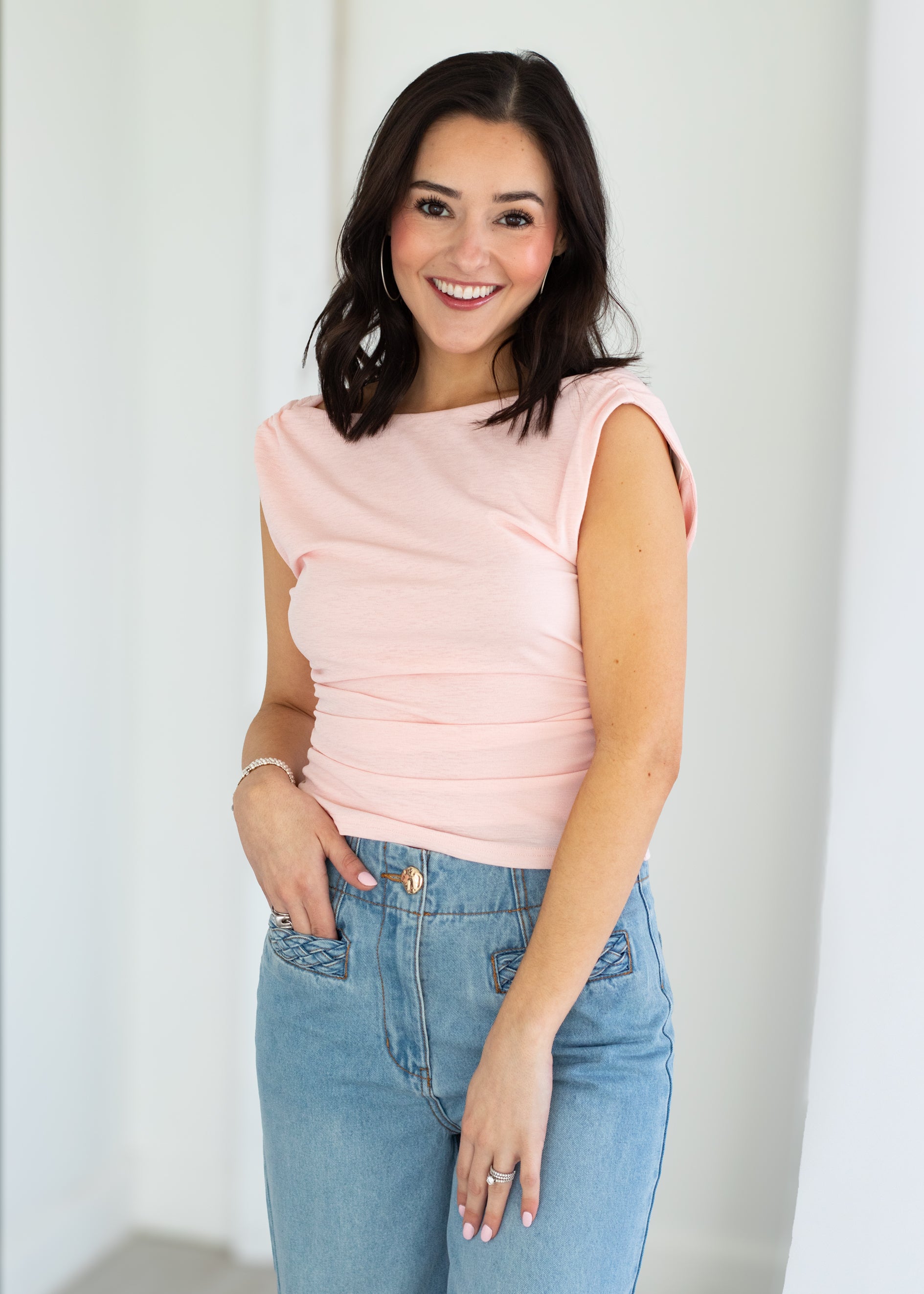 Woman wearing a light pink sleeveless top and blue jeans against a plain background