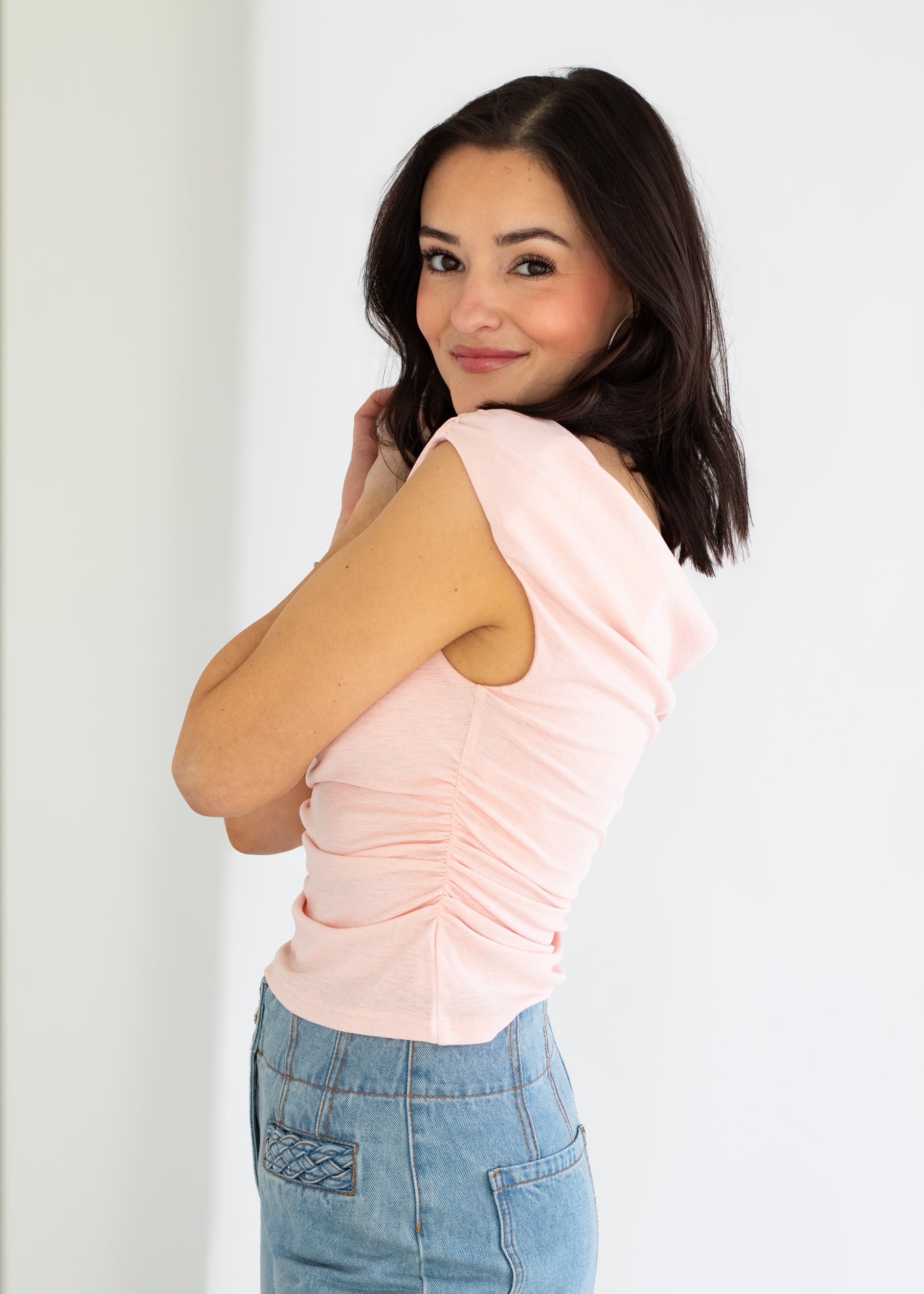 Woman wearing a light pink sleeveless top and blue jeans against a white background
