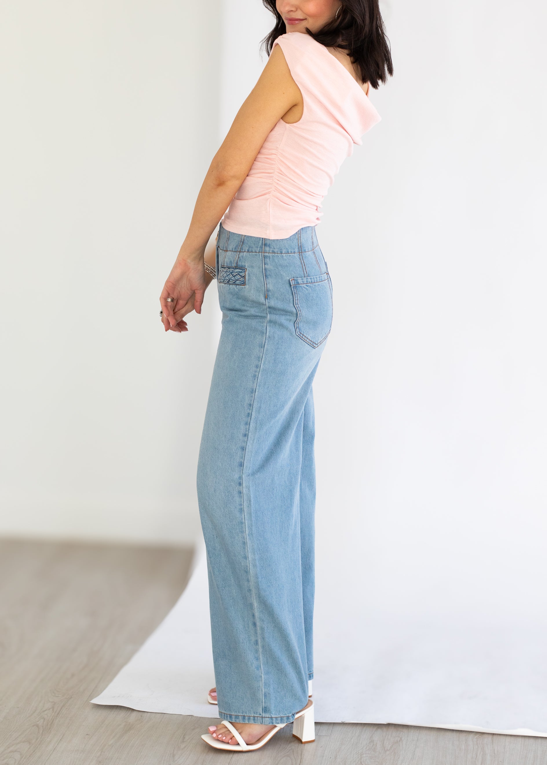 Woman wearing a pink sleeveless top and light blue jeans on a plain background