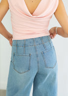 Person wearing a pink sleeveless top and blue jeans against a white background