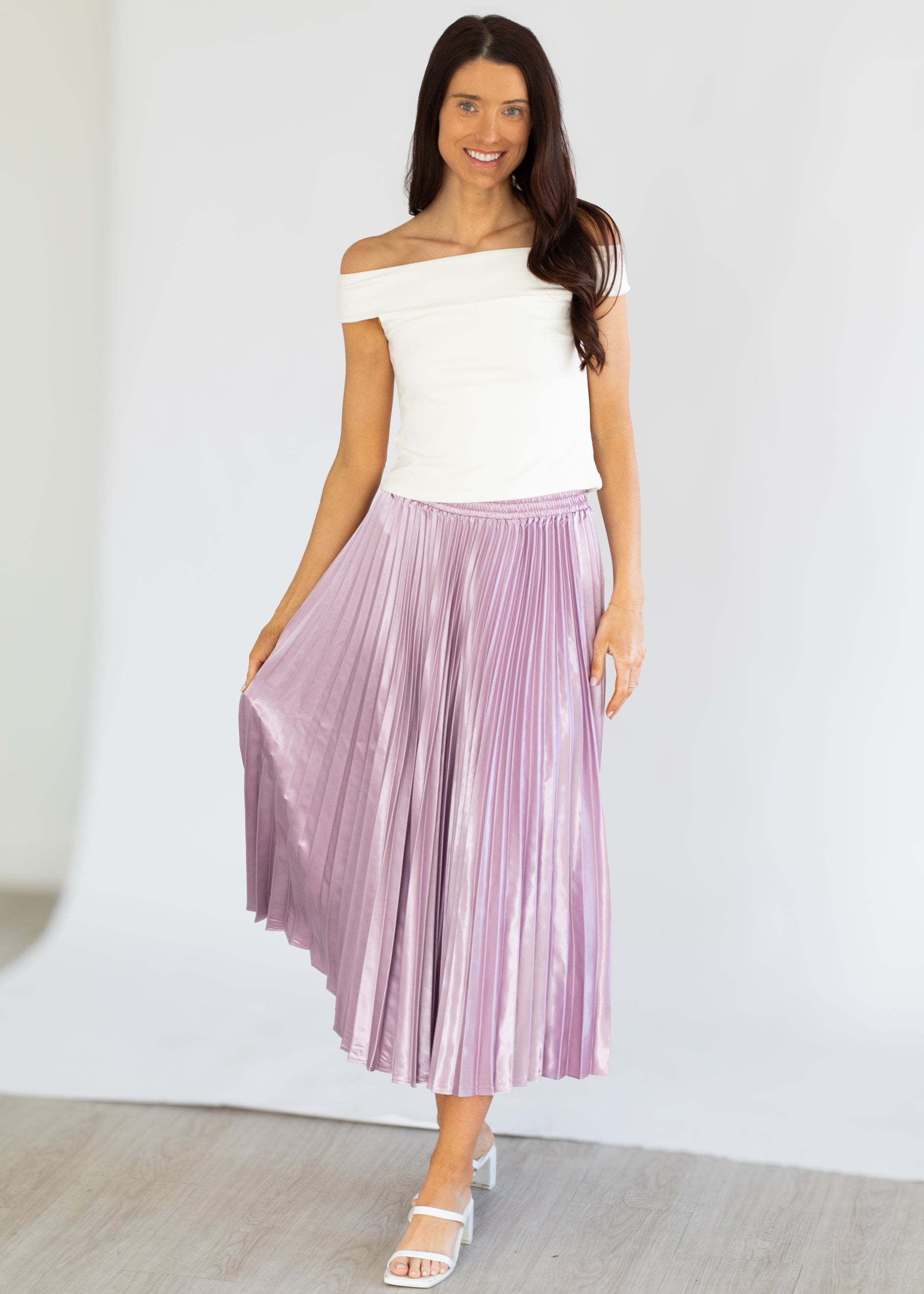 Woman wearing a white top and purple pleated skirt on a plain background