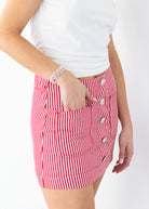 Red and white striped skirt with button details worn by a person on a white background