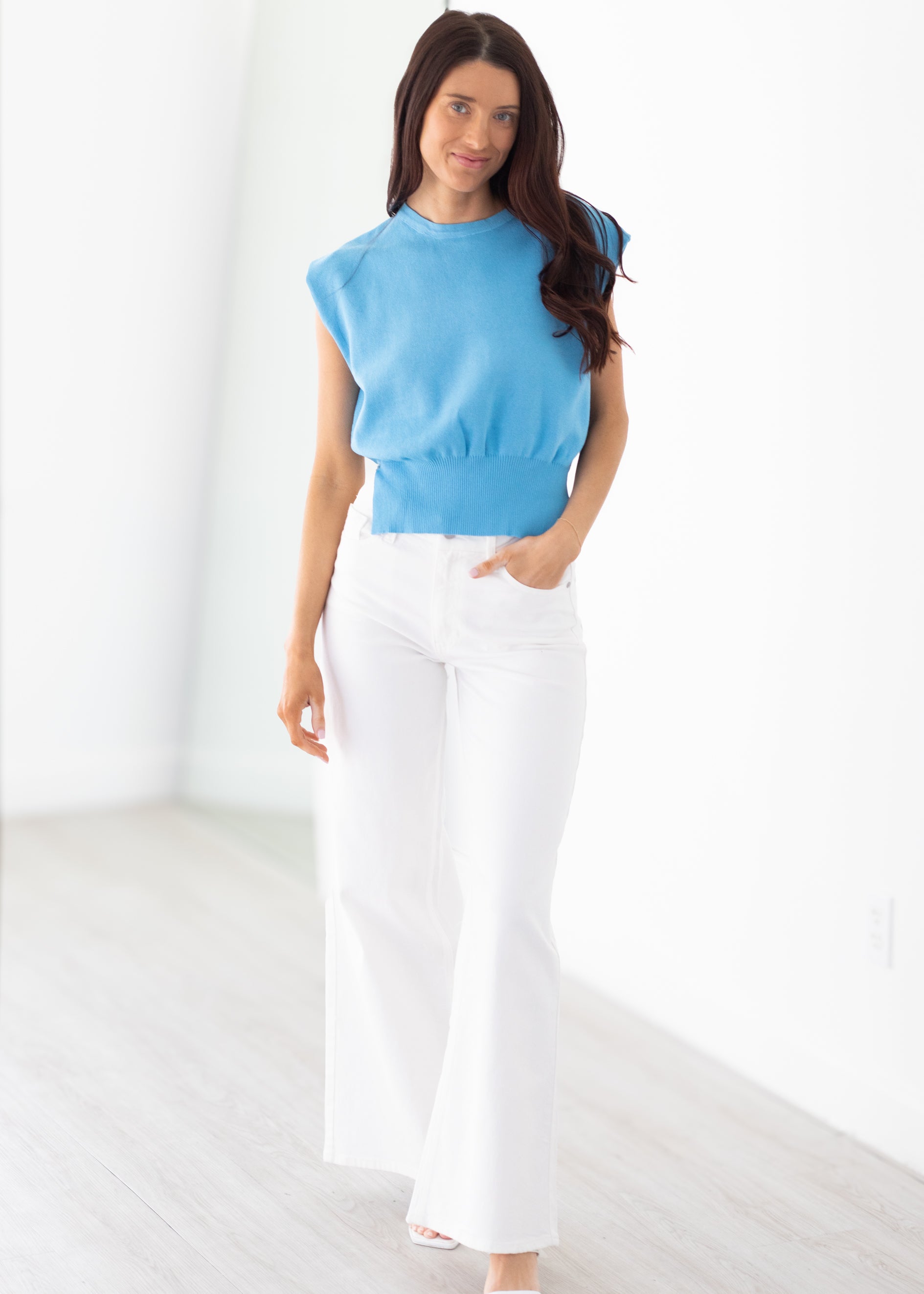 Woman wearing a blue top and white pants on a white background