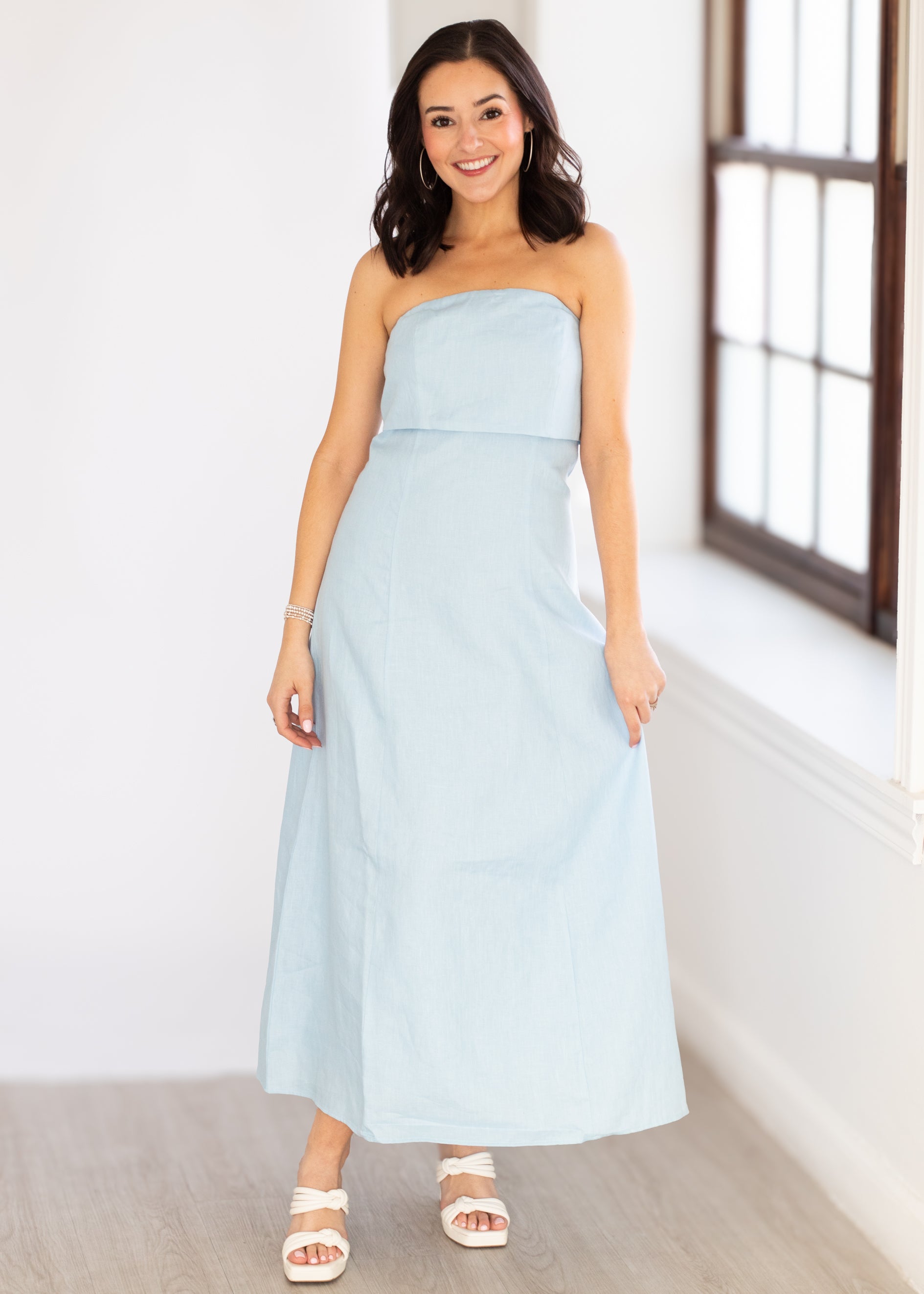 Woman wearing a light blue strapless dress in a bright room.