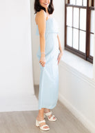 Woman in a light blue dress standing in a room with a window.