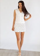 Woman wearing a white skirt with black polka dots against a plain background