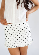 White skirt with black polka dots worn by a person on a plain background