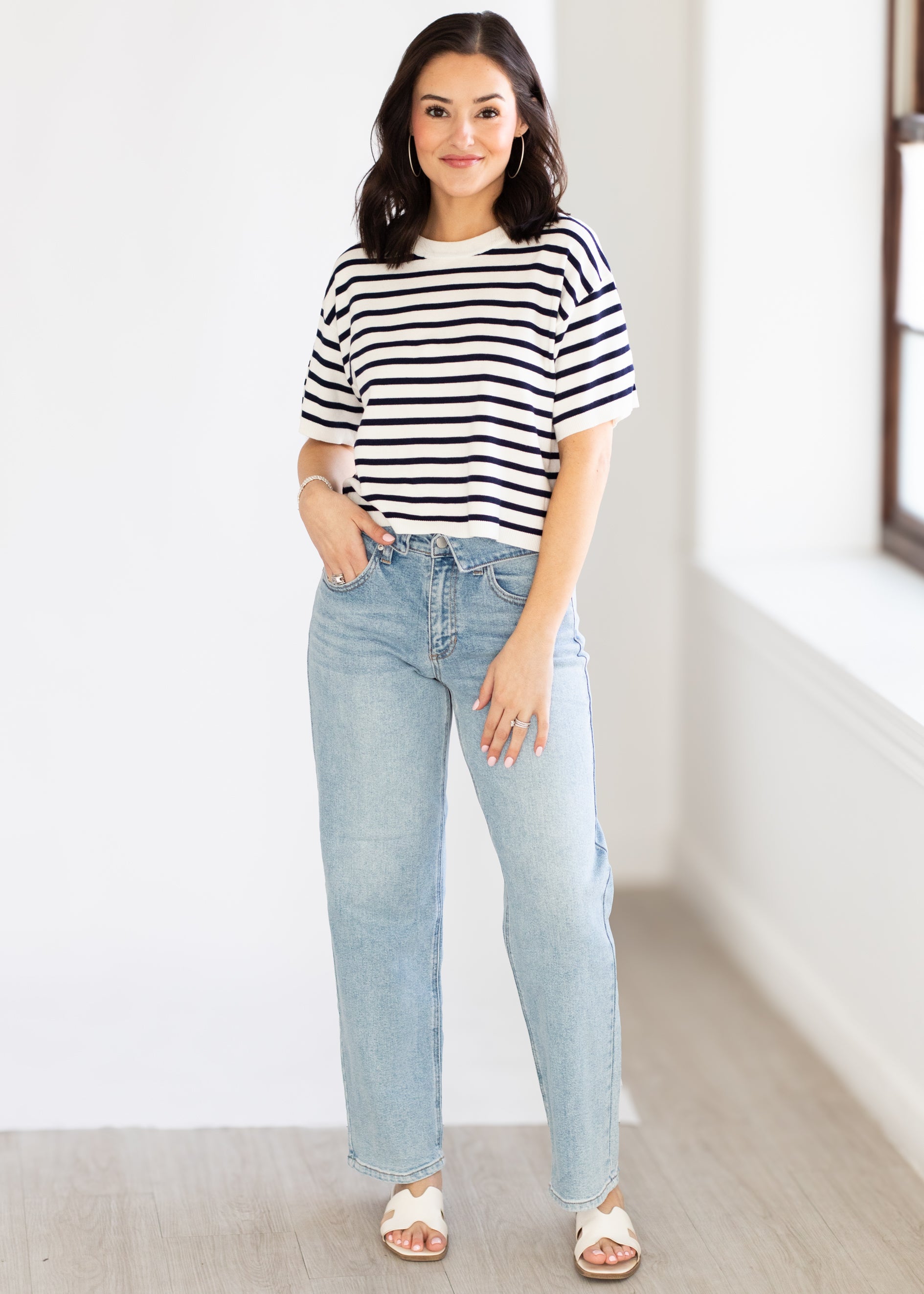 Woman wearing a navy and white striped shirt and light blue jeans indoors.