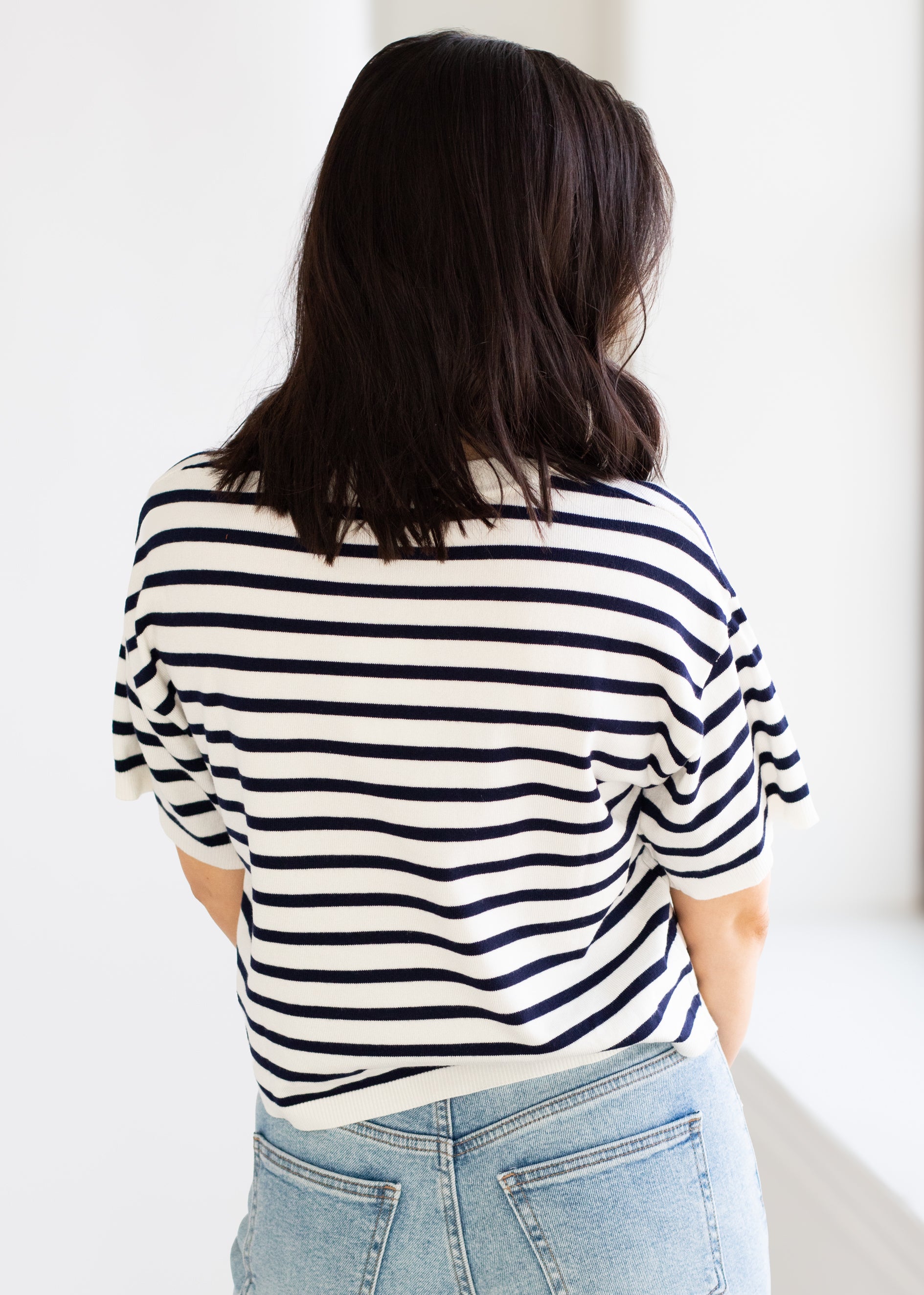 Person wearing a navy and white striped shirt and light blue jeans against a white background