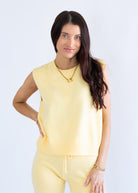 Woman wearing a yellow sleeveless top and pants on a light gray background