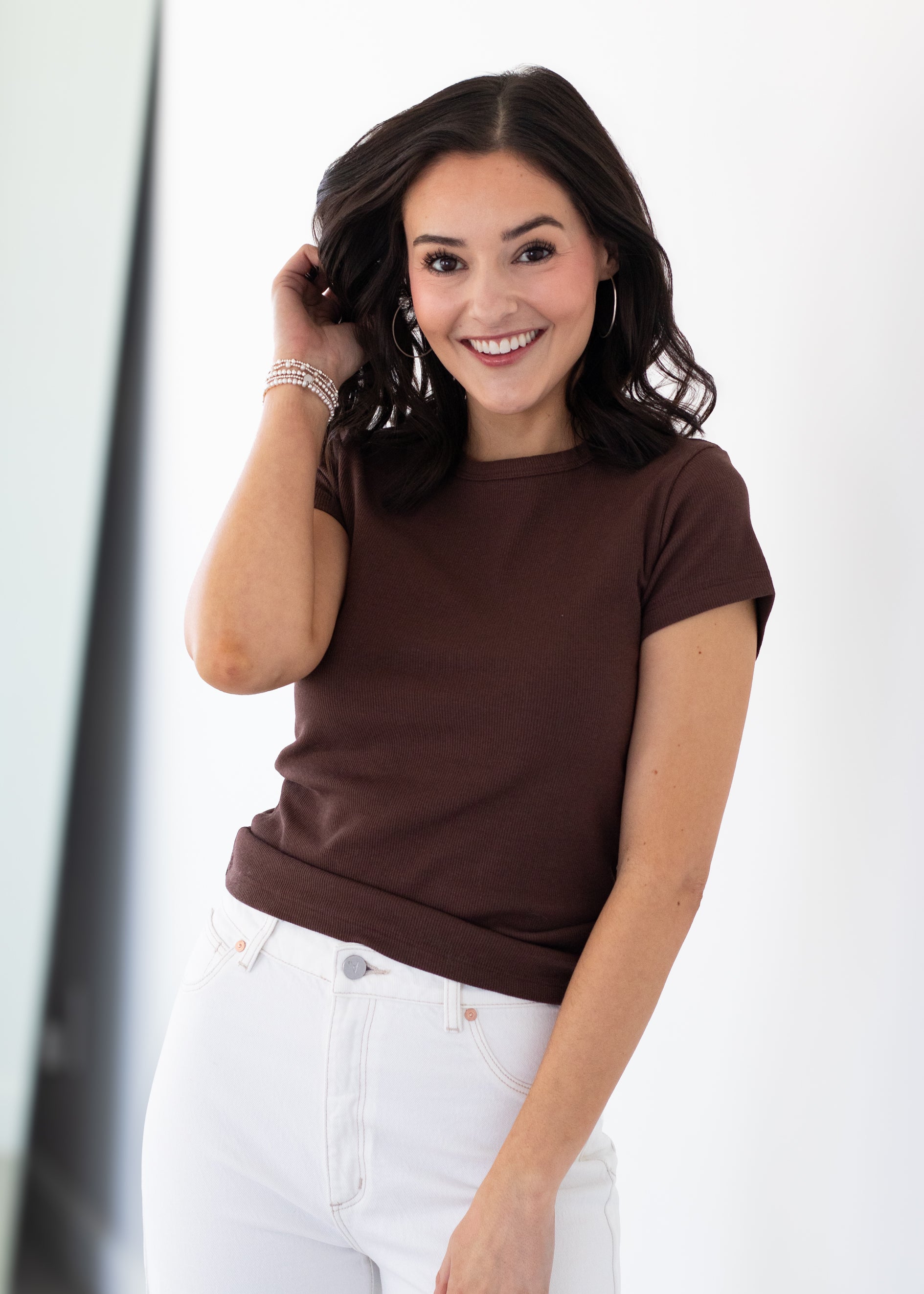 Woman wearing a brown t-shirt and white pants against a white background
