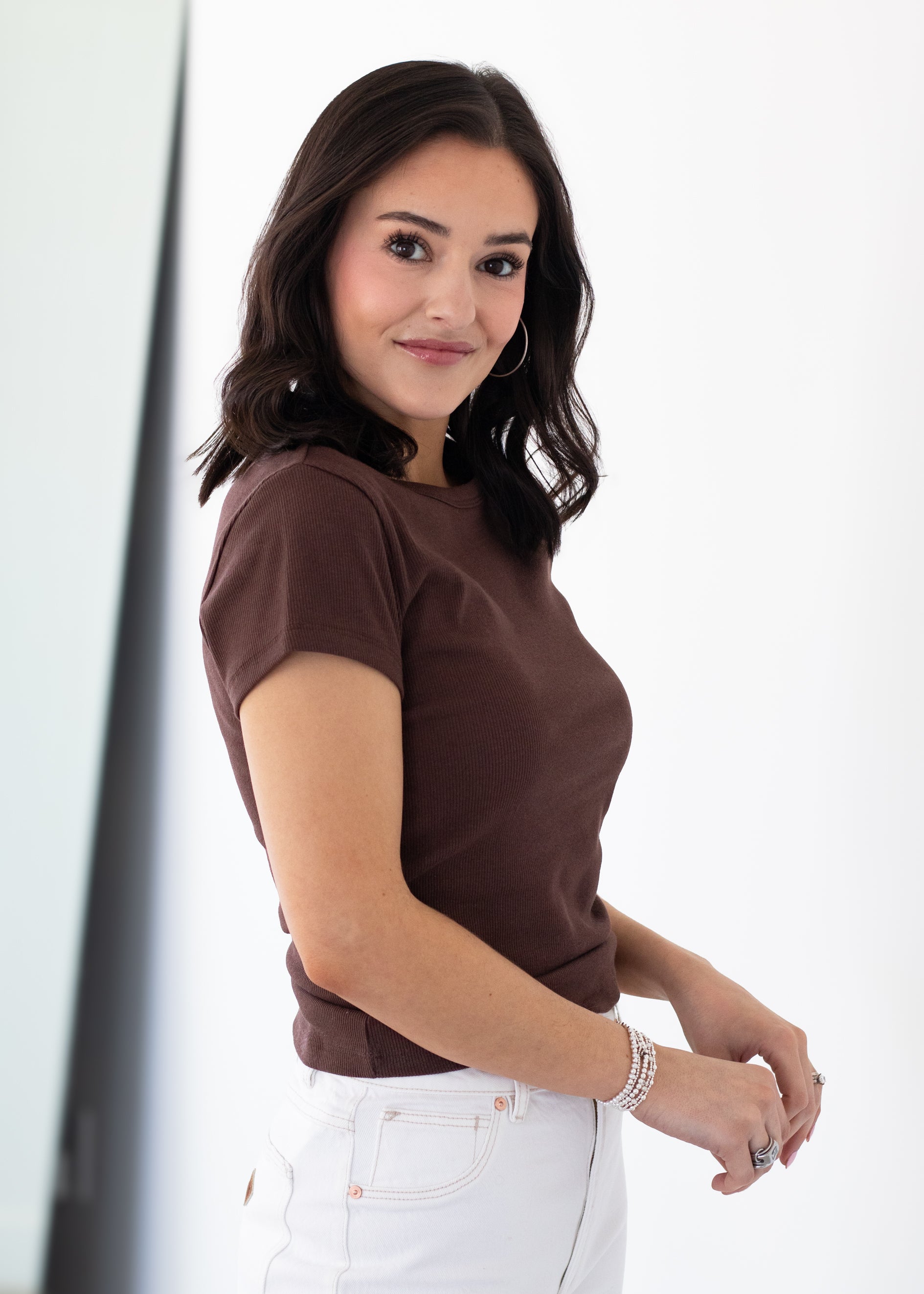 Woman wearing a brown top and white pants against a white background