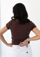 Person wearing a brown t-shirt and white pants on a plain background