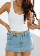 Person wearing a white tank top and blue denim skirt with gold jewelry.