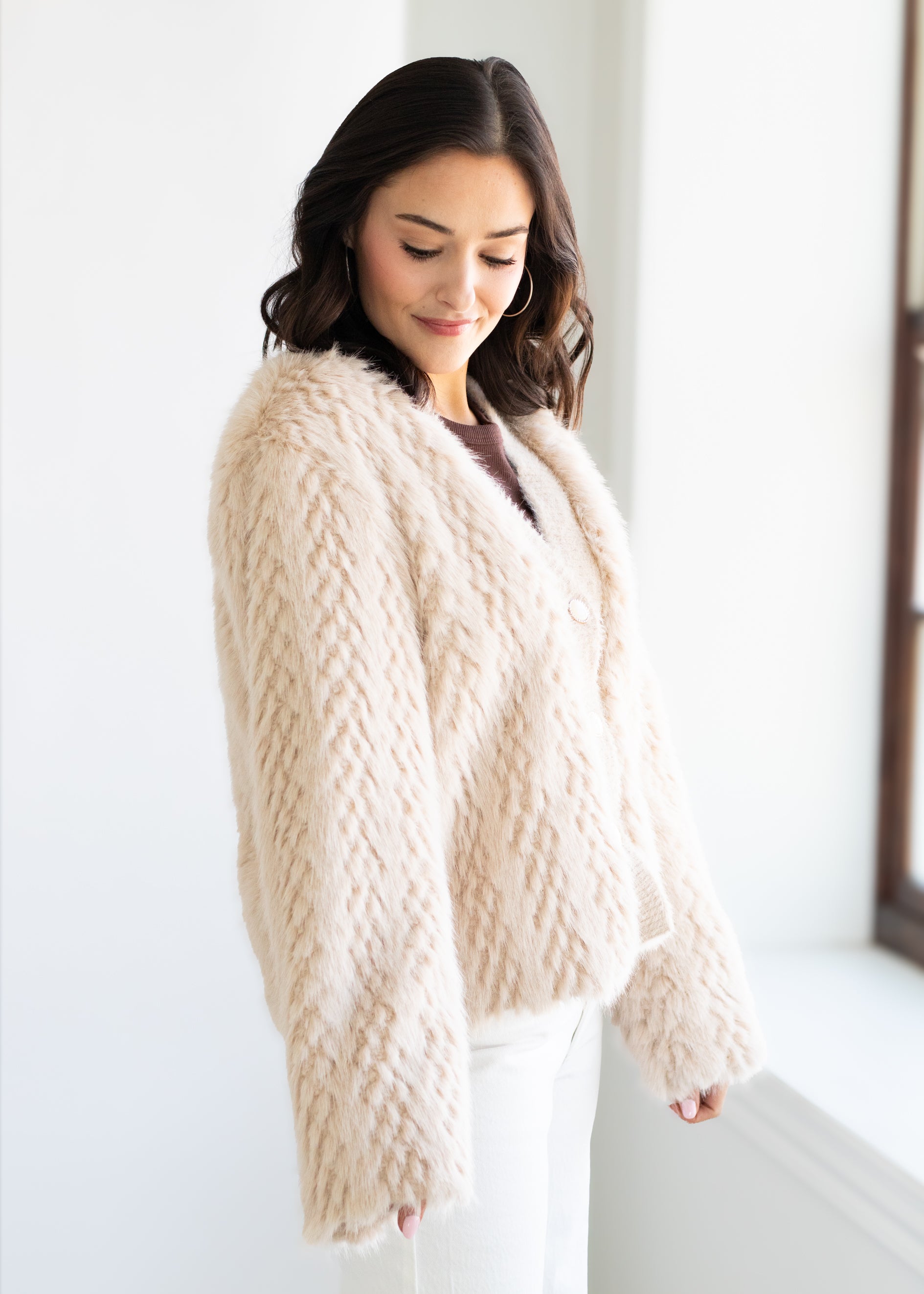 Woman wearing a beige knitted cardigan in a bright room.