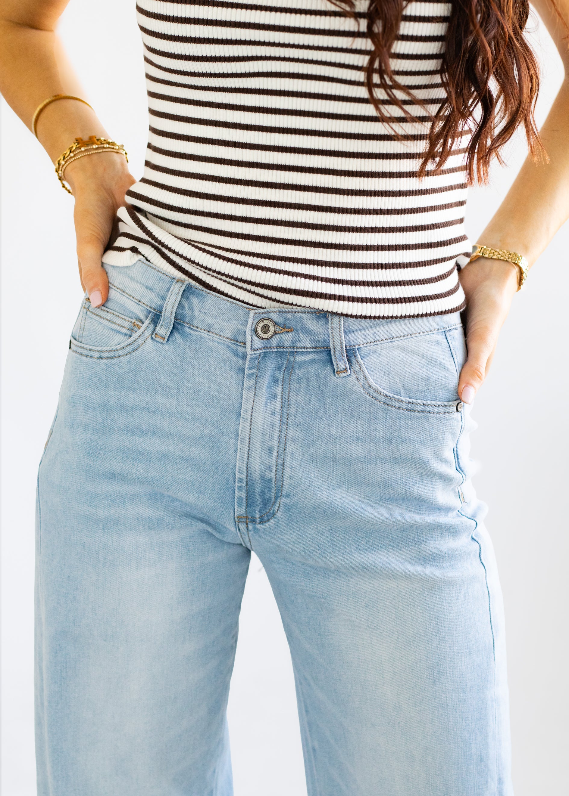 Person wearing a striped top and light blue jeans with hands in pockets on a white background