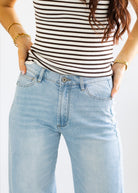 Person wearing a striped top and light blue jeans with hands in pockets on a white background