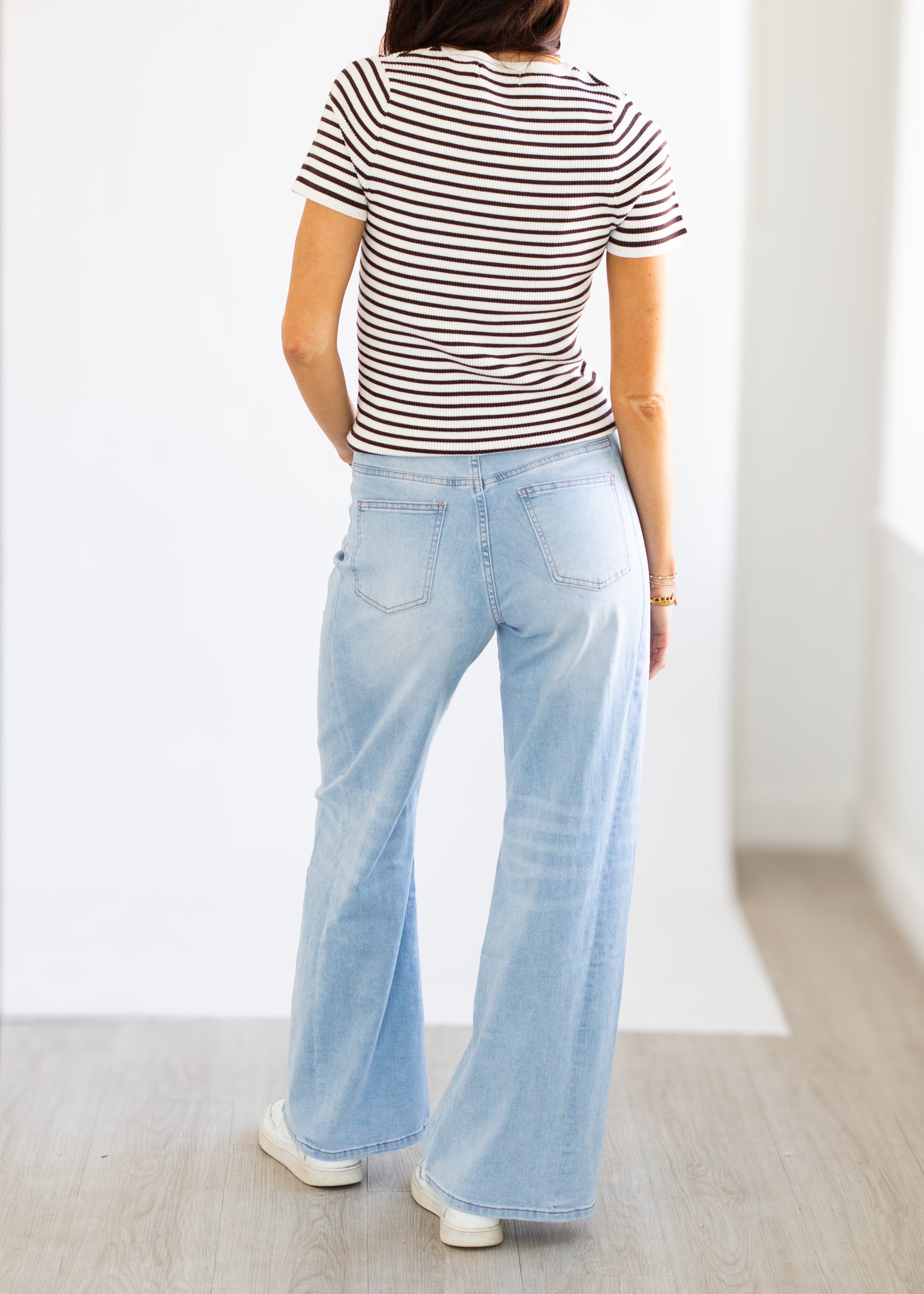 Person wearing a striped shirt and light blue jeans on a plain background