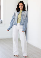 Woman wearing a denim jacket, yellow top, and white pants indoors.