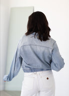 Person wearing a light blue denim jacket and white pants in a minimal indoor setting